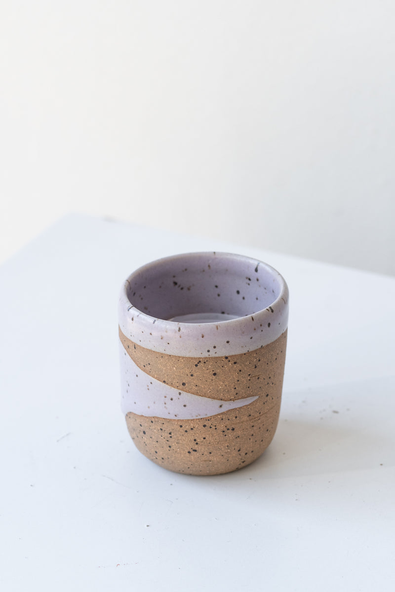 Lavender Coastal Glaze Cup by Christina Kosinski sits on a white surface in a white room