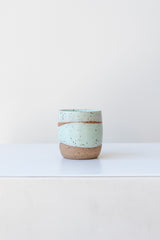 Mint Coastal Glaze Cup by Christina Kosinski sits on a white surface in a white room