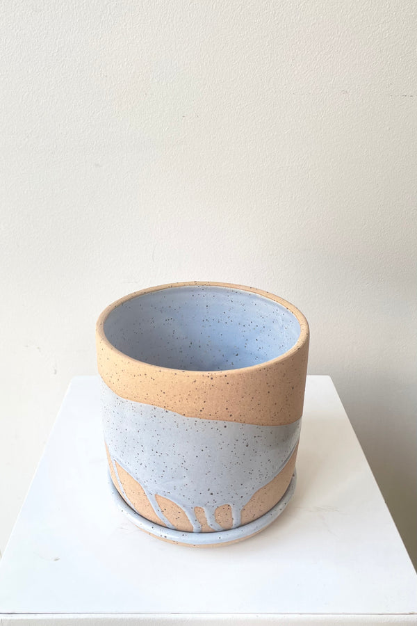 A slight over-the-lip view of the handmade 4.5" cylinder pot and saucer in blue splash against a white backdrop 