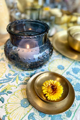 Blue Hobnail Round Vase with a candle inside set on a table cloth and a gold dinner set