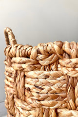 A close-up view of the medium Handwoven Seagrass & Metal Basket with handles against a white backdrop