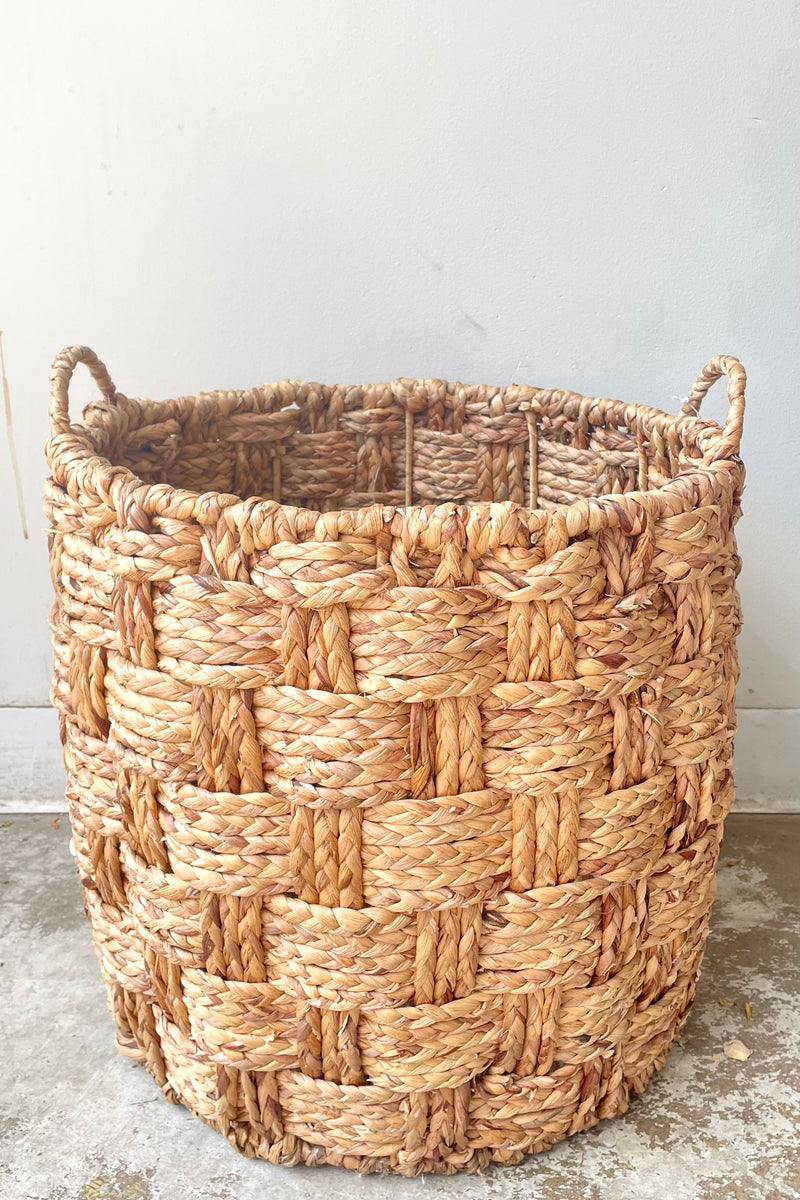 A frontal view of the medium Handwoven Seagrass & Metal Basket with handles against a white backdrop