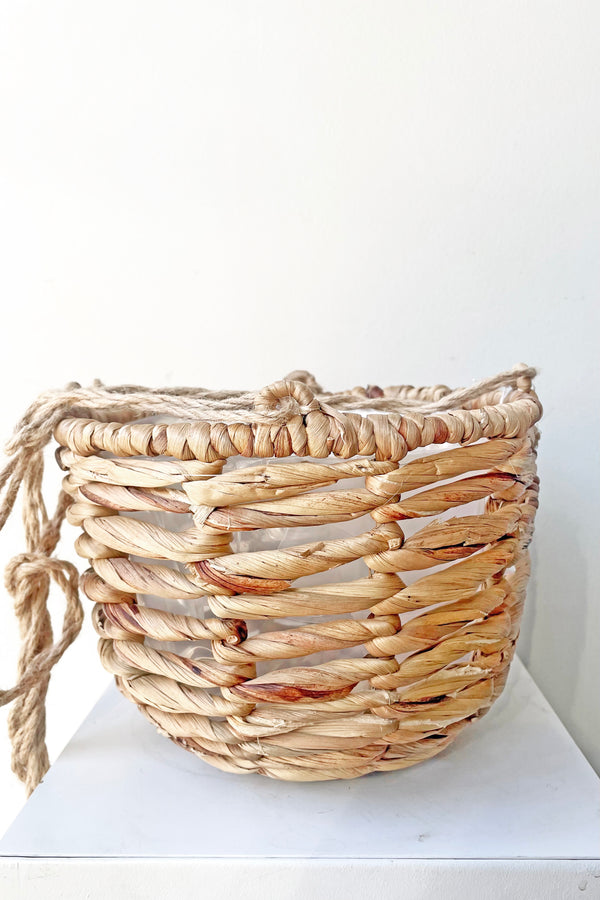 Water Hyacinth Hanging Basket medium sits on a white pedestal 