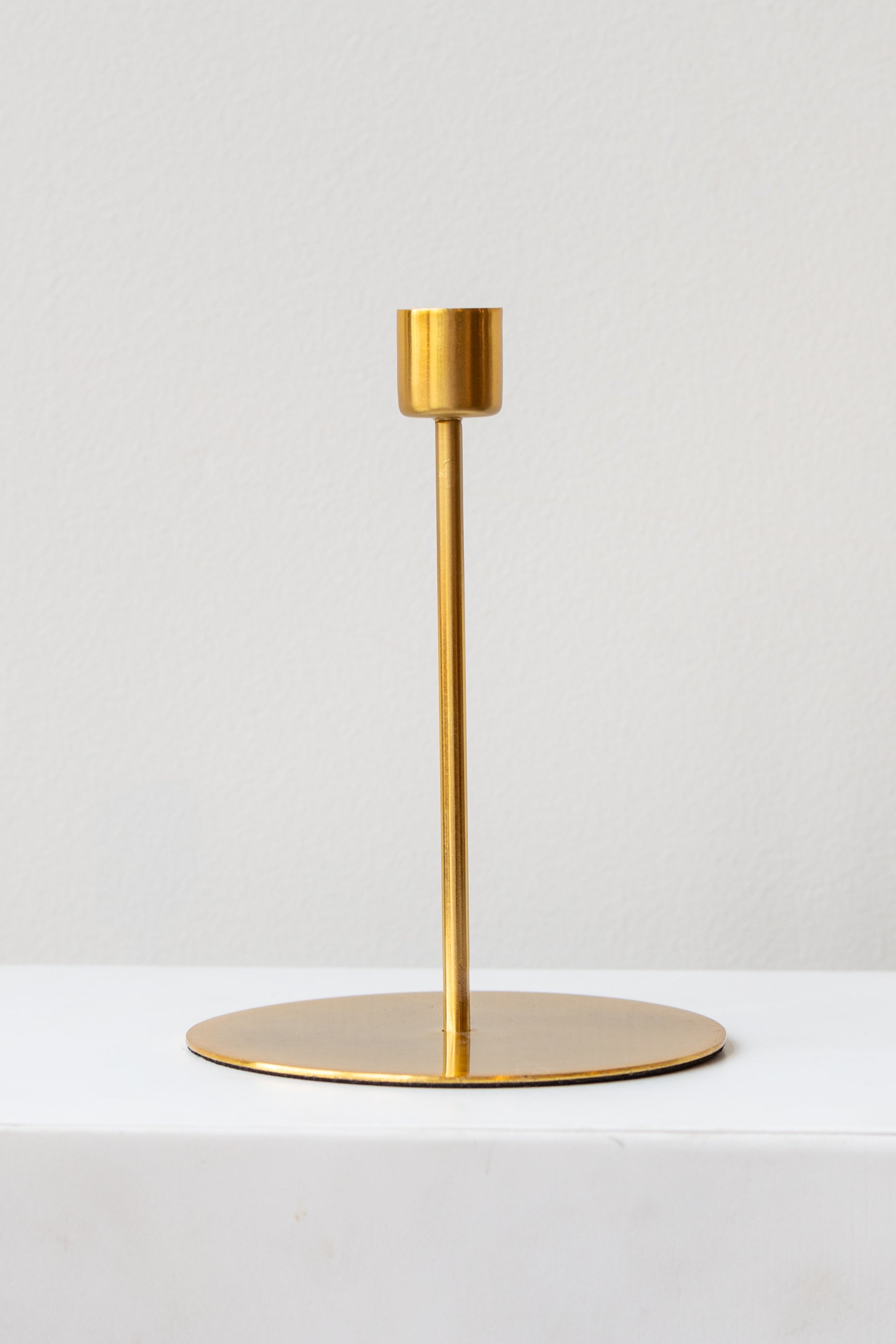 Gold tall taper candle holder on a white surface in a white room