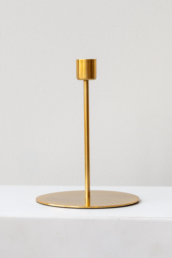 Gold tall taper candle holder on a white surface in a white room