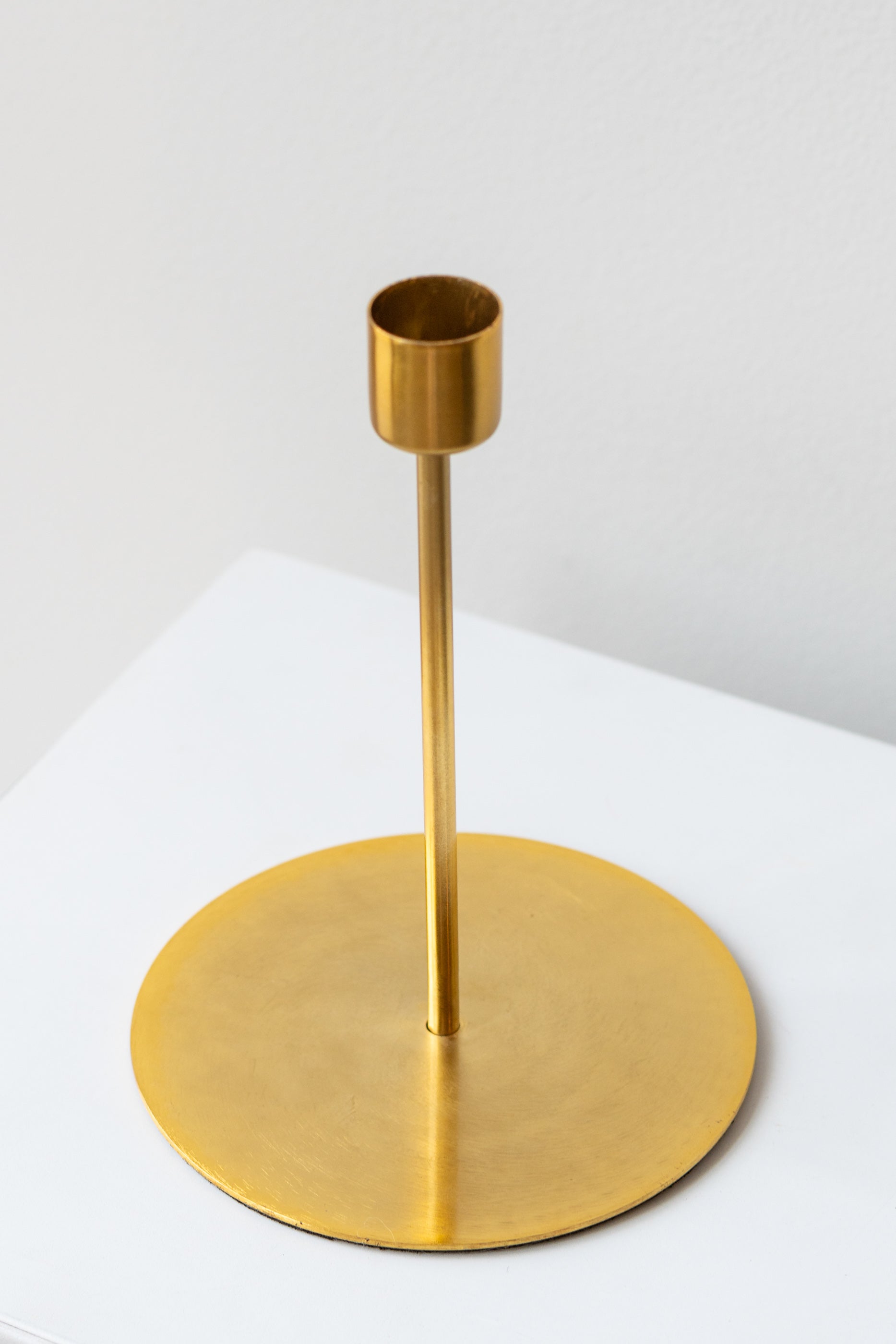 Gold tall taper candle holder on a white surface in a white room