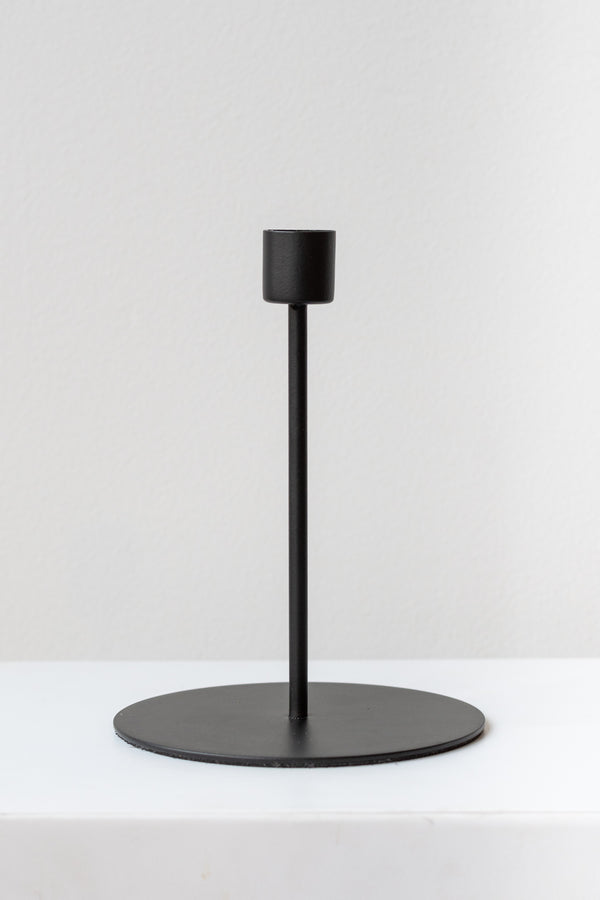 Black tall taper candle holder on a white surface in a white room