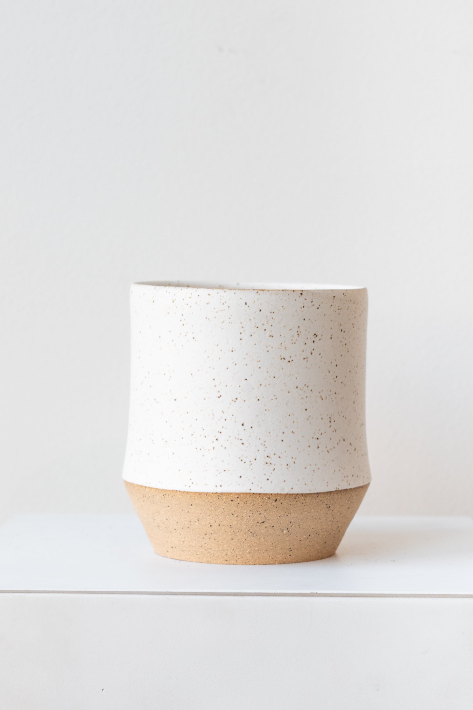 Megan Suave Ceramics small speckle stoneware vase on a white surface in a white room