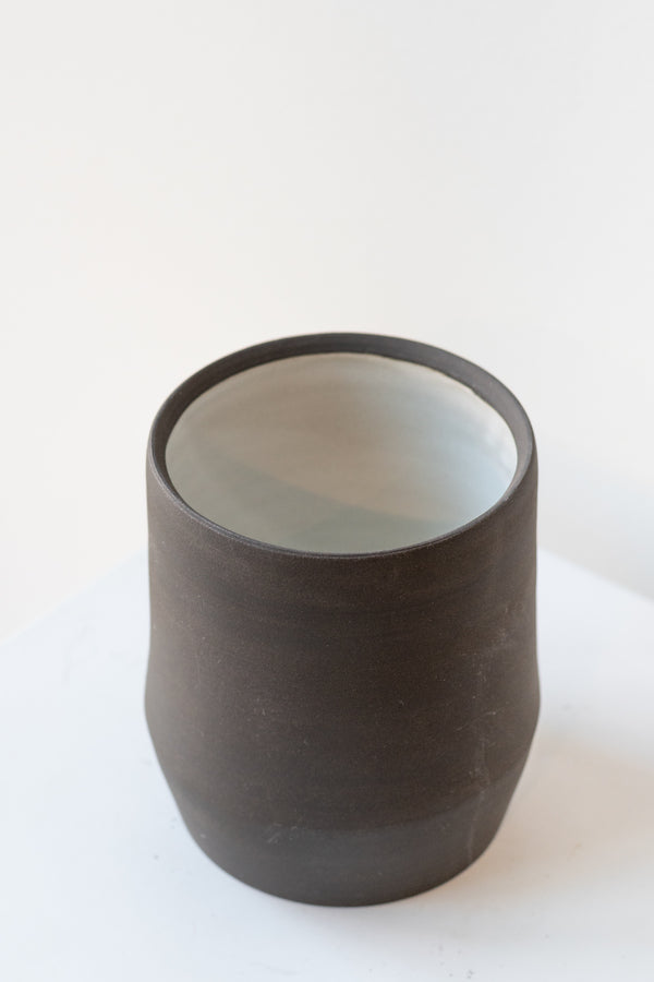Megan Suave Ceramics small black stoneware vase on a white surface in a white room