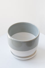 Two-toned grey and white ceramic kinto planter and saucer on a white surface in a white room