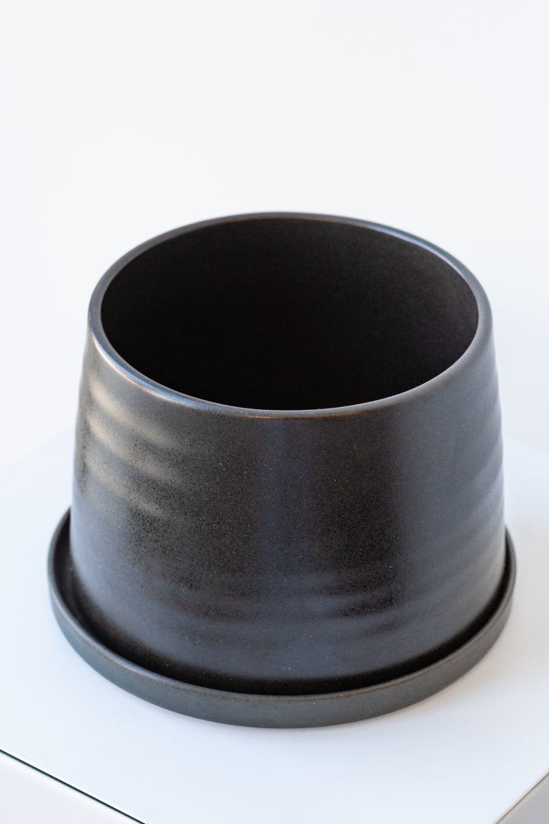 Large black KINTO porcelain planter pot on a white surface in a white room