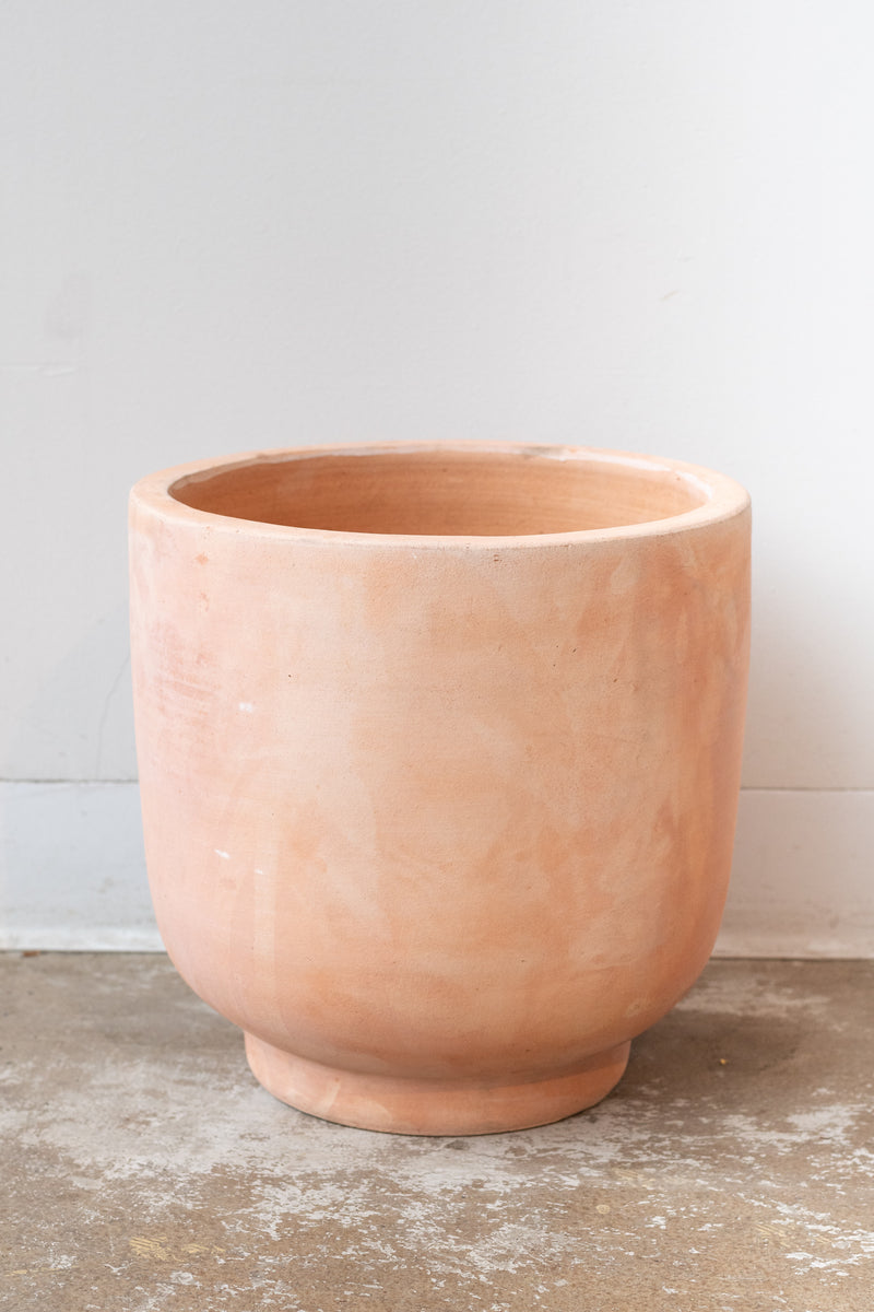 Large footed terra cotta planter by Hawkins New York on a white surface in a white room