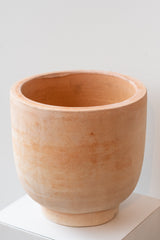 Medium footed terra cotta planter by Hawkins New York on a white surface in a white room