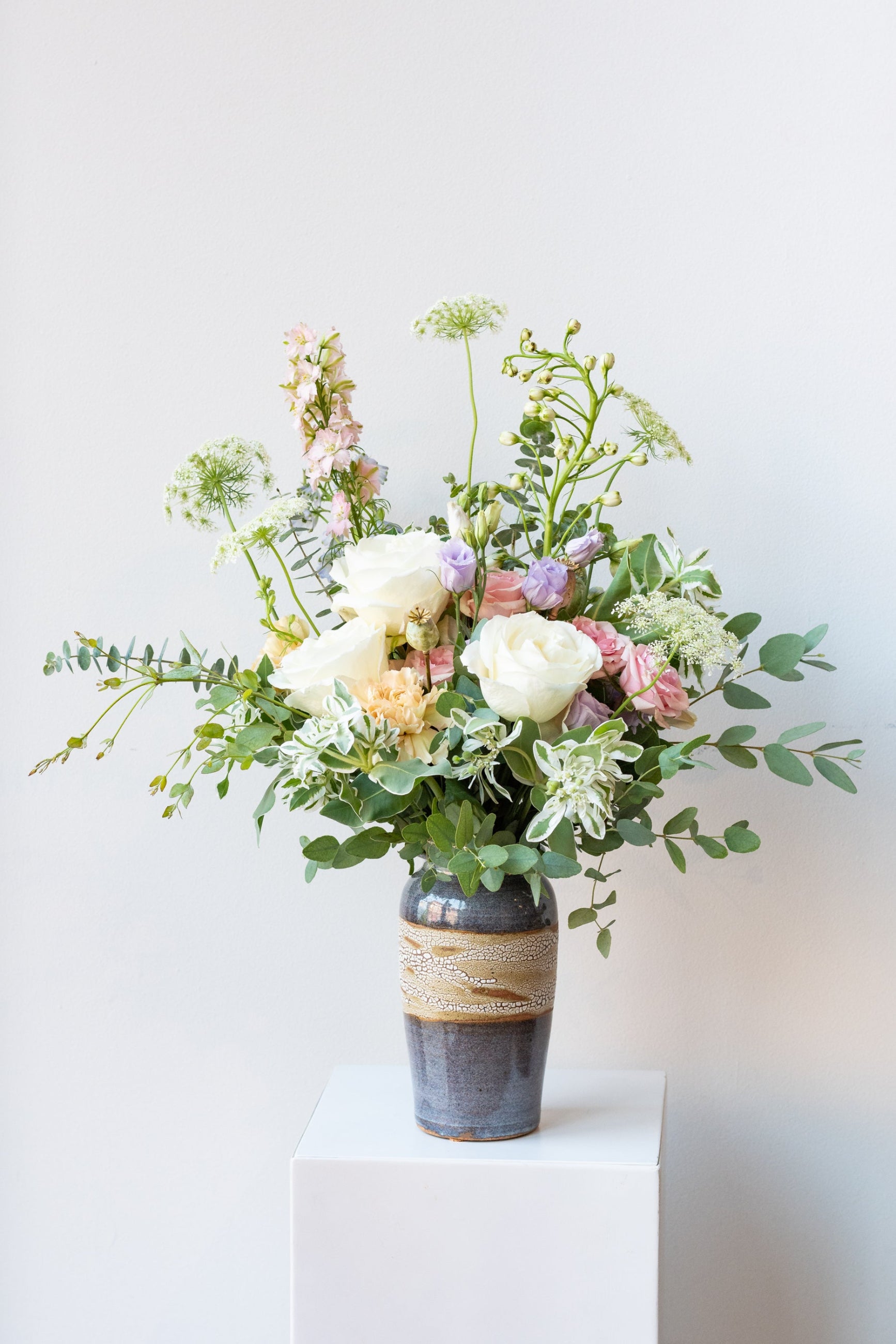 Dawn floral arrangement by Sprout Home sits in a blue ceramic vase on a white pedestal in a white room ©Sprout Home #size_$100