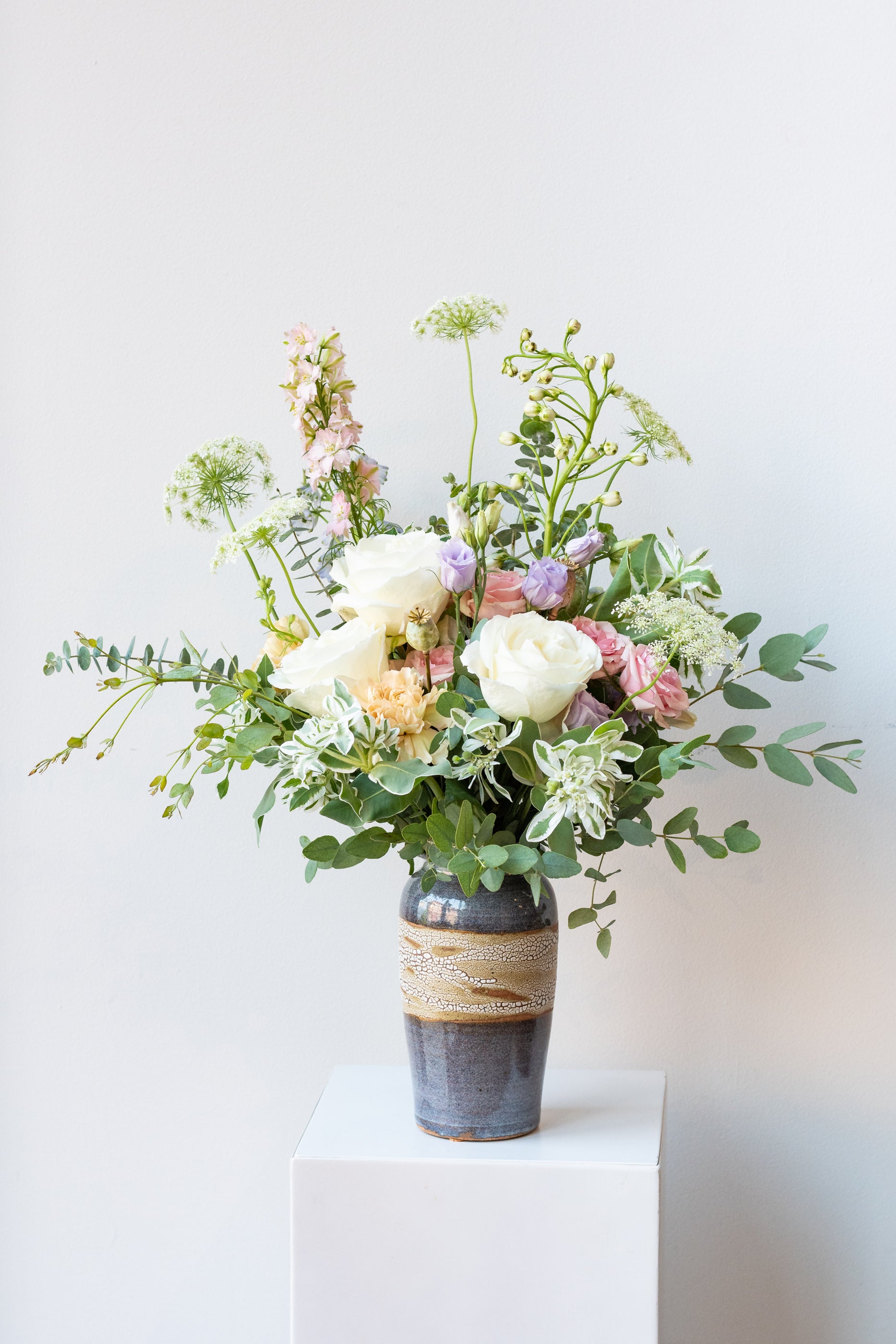 Dawn floral arrangement by Sprout Home sits in a blue ceramic vase on a white pedestal in a white room #size_$90