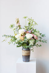 Dawn floral arrangement by Sprout Home sits in a blue ceramic vase on a white pedestal in a white room