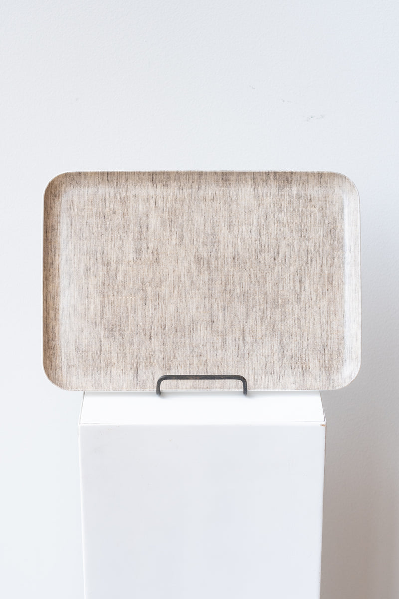 Natural linen coated serving tray by Fog Linen on a white pedestal in front of white background