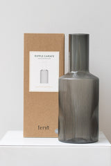 Ferm living Ripple Carafe glass smoke next to its box on a white surface in a white room