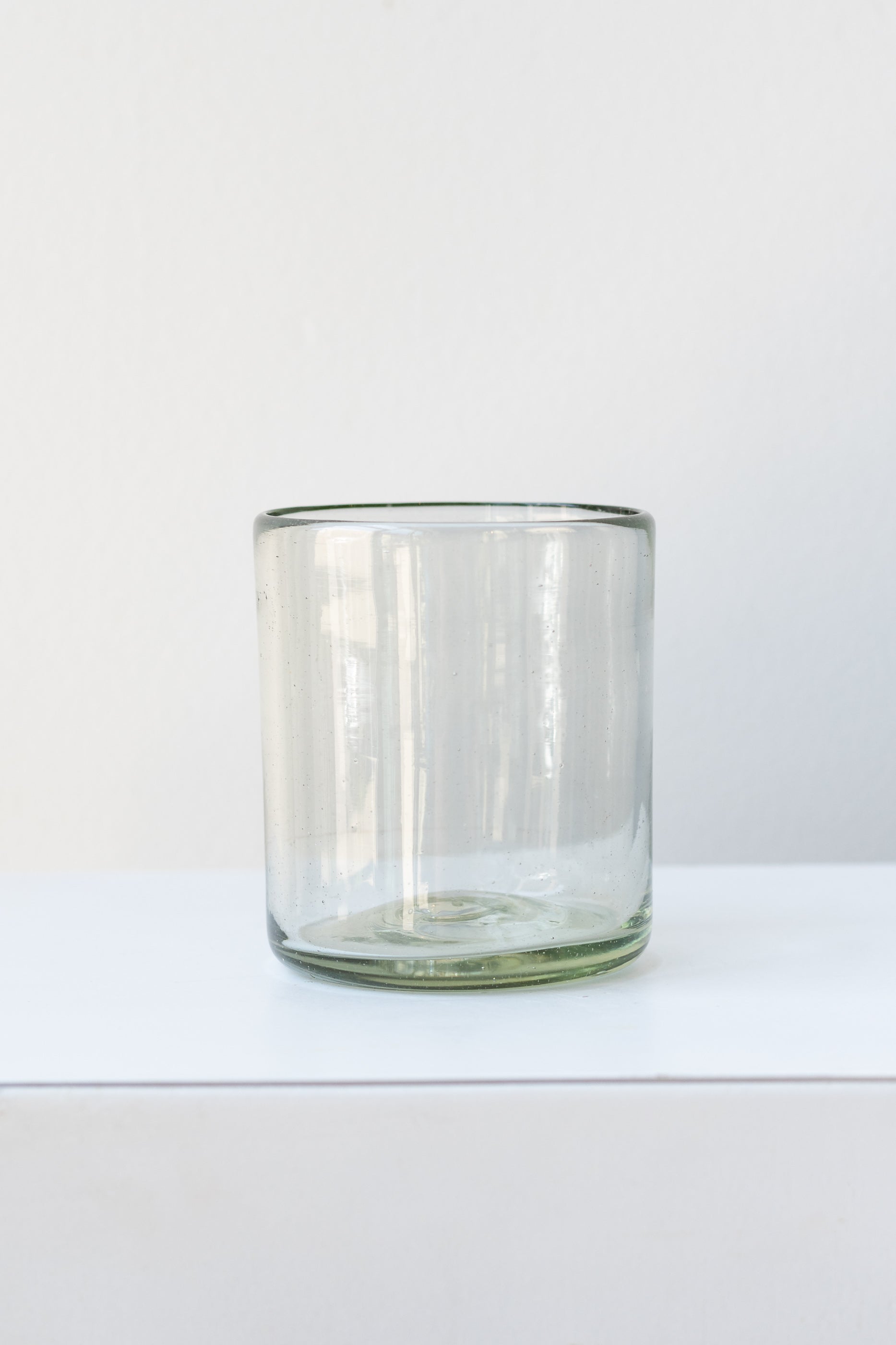 Recycled hand-blown rocks tumbler glass on white surface in a white room