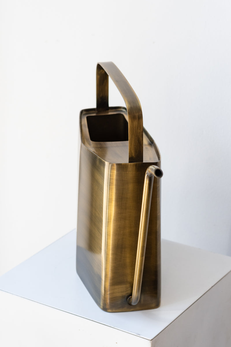Modern brass watering can by Modern Sprout on white pedestal in front of white background