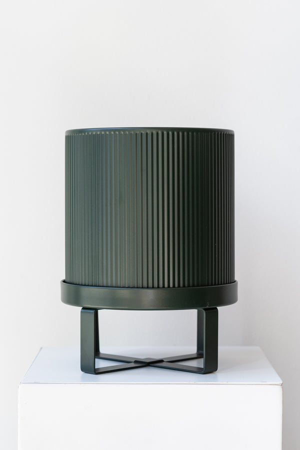 Small dark green Bau Pot by Ferm Living on a white pedestal in front of white background