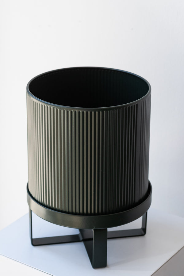 Small dark green Bau Pot by Ferm Living on a white pedestal in front of white background