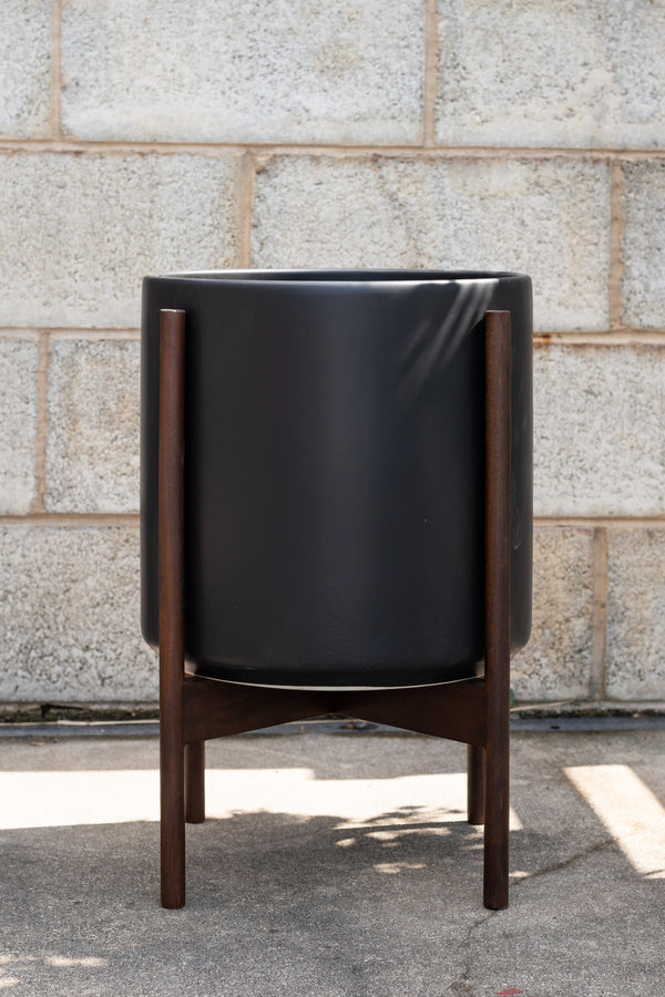 LBE Designs Stoneware Cylinder & Dark Teak Stand black 12” in front of concrete brick wall