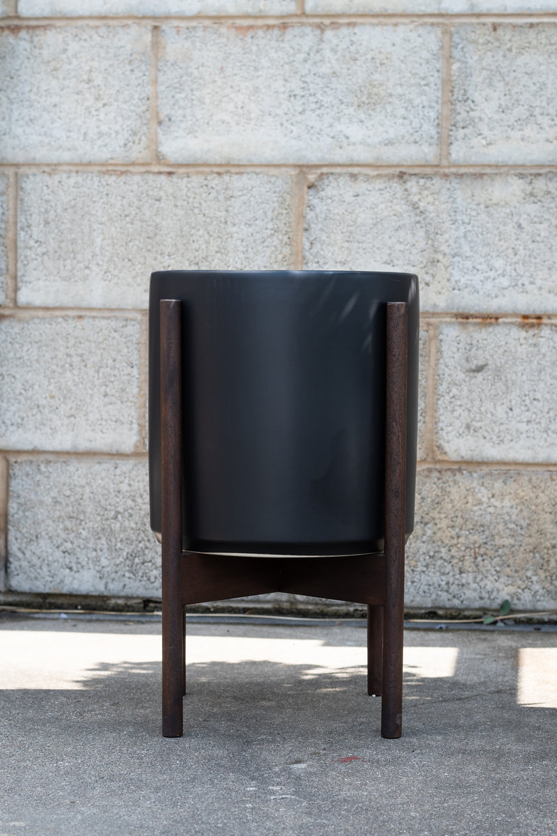 LBE Designs Stoneware Cylinder & Dark Teak Stand black 10” in front of concrete brick wall