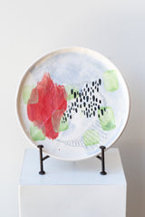 Red fields porcelain painted platter by Technicolor Dino in black iron plate stand on a white pedestal in a white room