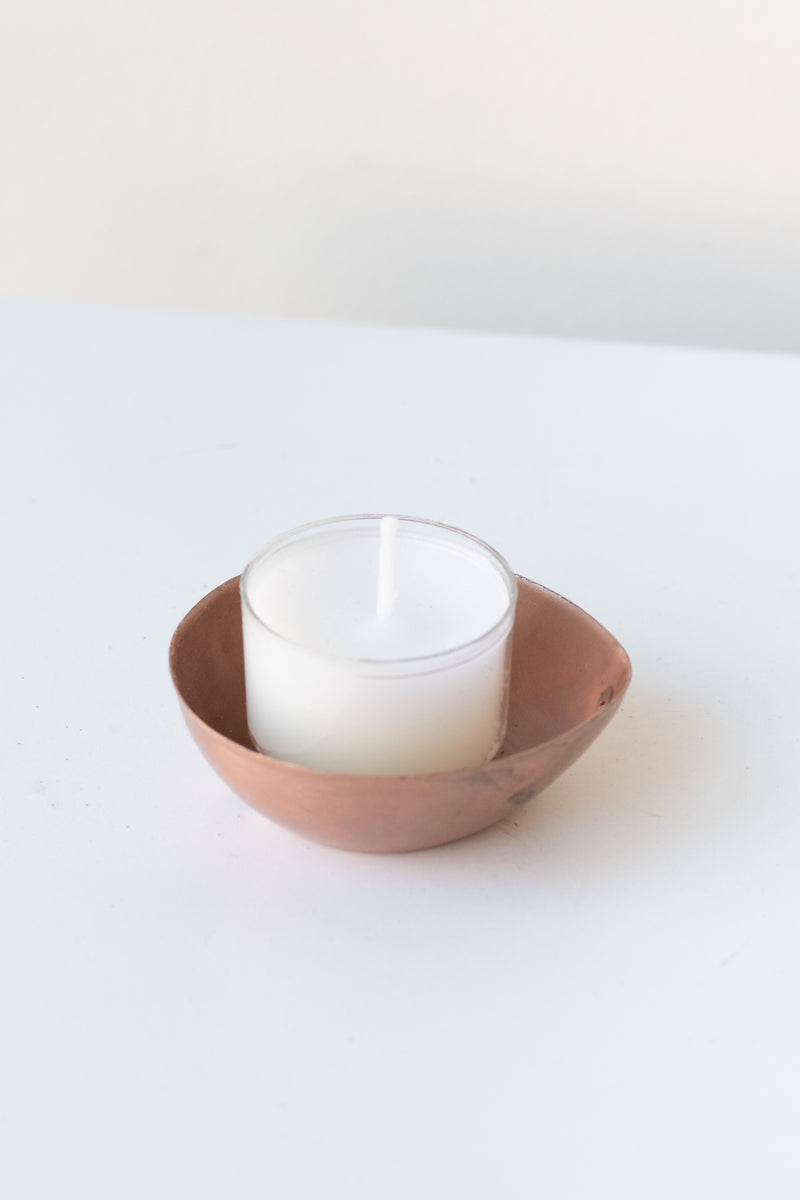 Alma Copper Tealight Holder on a white surface in a white room. Inside the holder is a white unlit tealight candle
