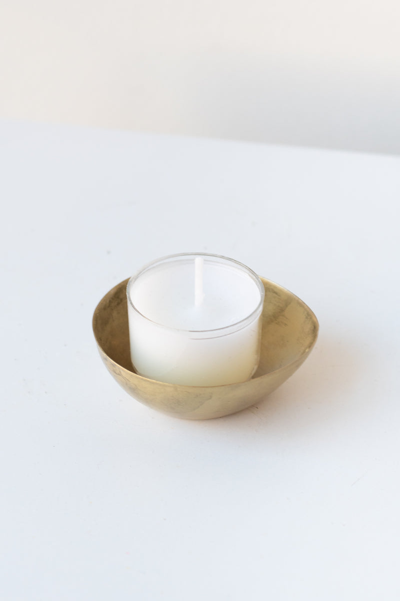 Alma Brass Tealight Holder on a white surface in a white room. Inside the holder is a white unlit tealight candle