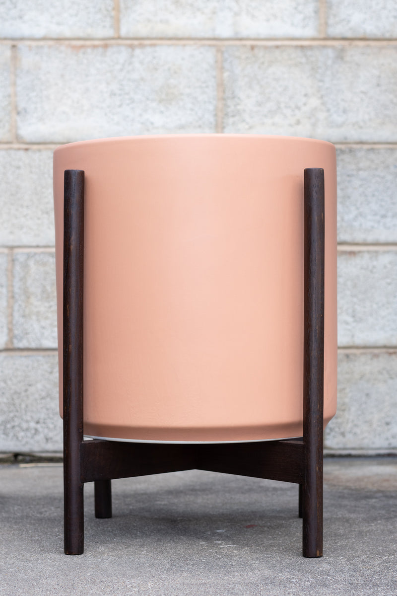 LBE Designs The 14 Cylinder & Dark Teak Stand peach in front of concrete wall