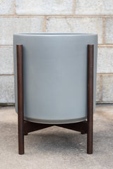 LBE Designs The 14 Cylinder & Dark Teak Stand gray in front of concrete wall