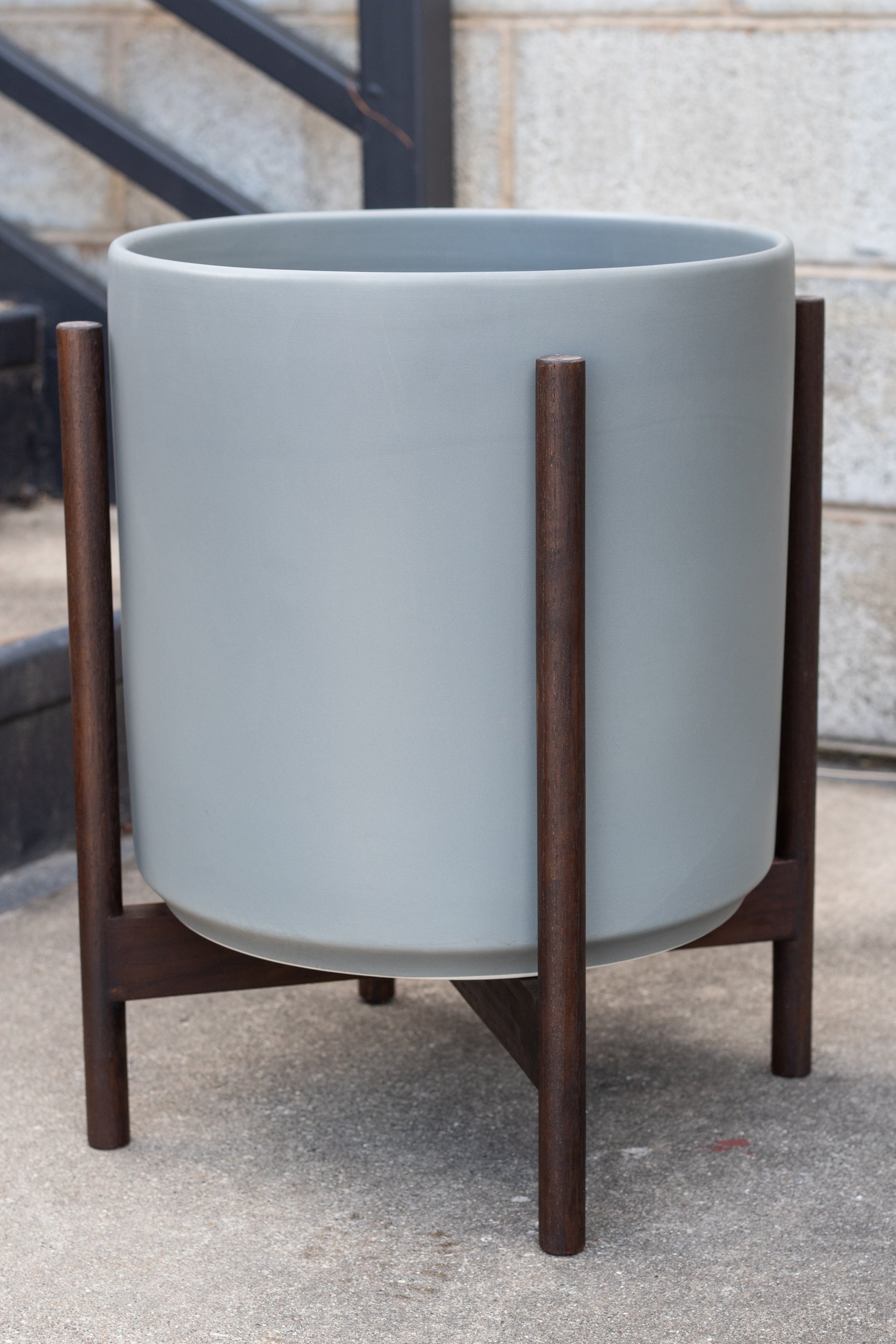 LBE Designs The 14 Cylinder & Dark Teak Stand gray in front of concrete wall