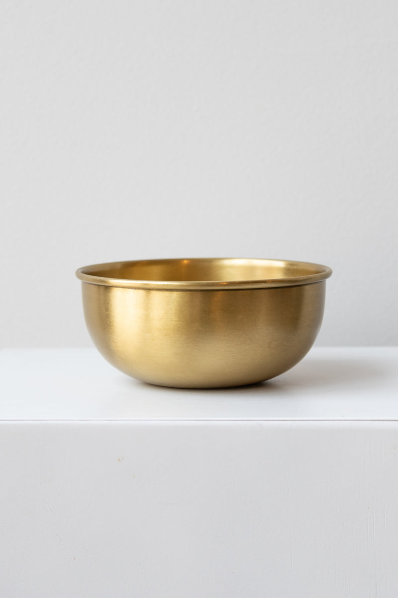 Large brass bowl by Fog Linen work sits on a white surface in a white room