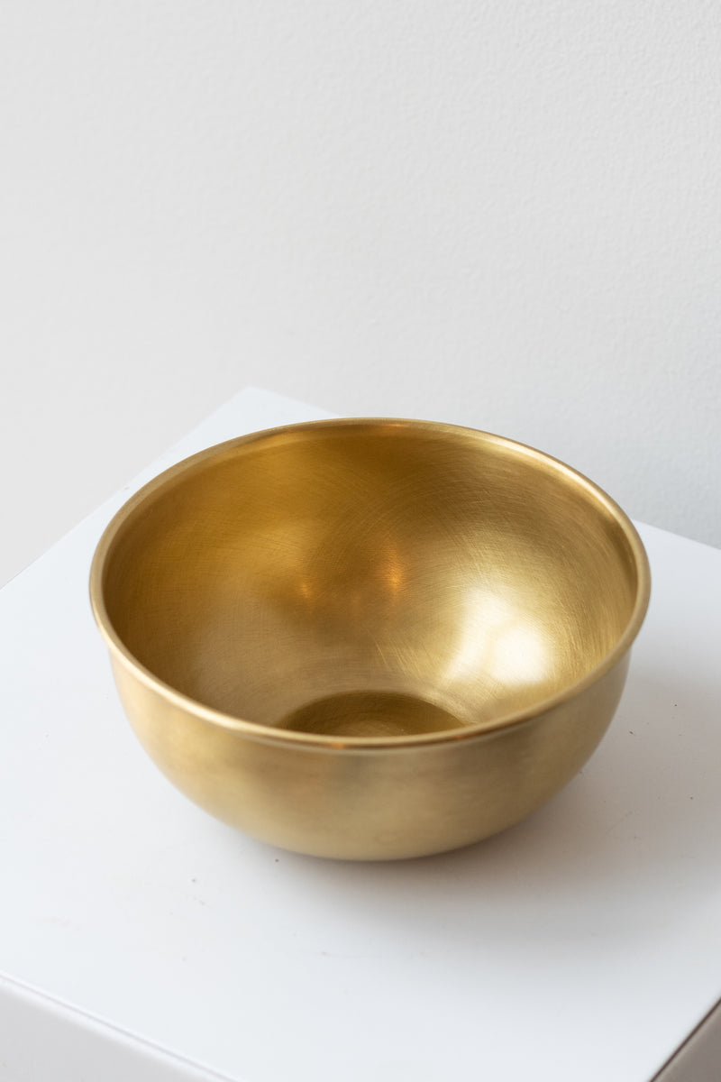 Large brass bowl by Fog Linen work sits on a white surface in a white room
