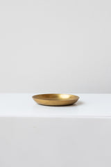 Extra small brass plate by Fog Linen Work sits on a white surface in a white room
