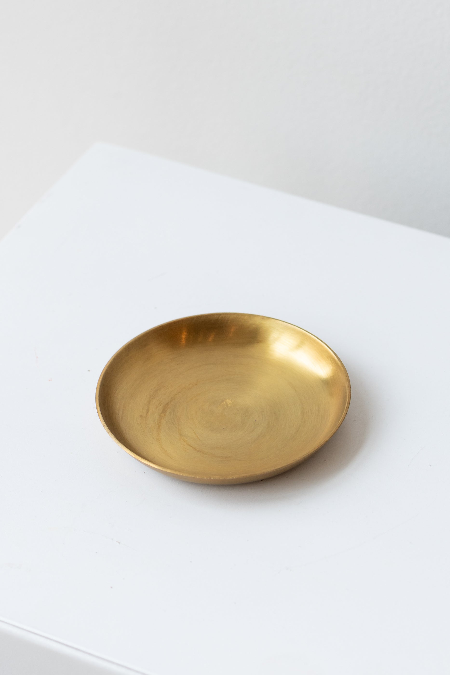 Extra small brass plate by Fog Linen Work sits on a white surface in a white room