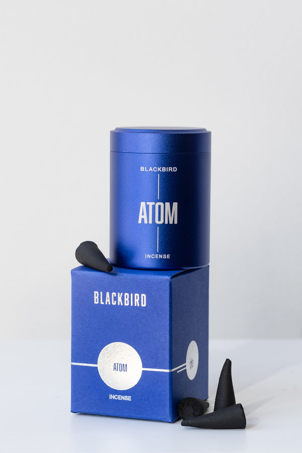 Box of Atom incense by Blackbird in front of white background. To the right of the box is a small pile of three incense cones, and on top of the box is a single incense cone on its side and the blue metal tin of incense