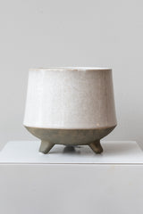 Glazed white stoneware planter with unglazed grey feet and base sits on a white surface in front of a white background