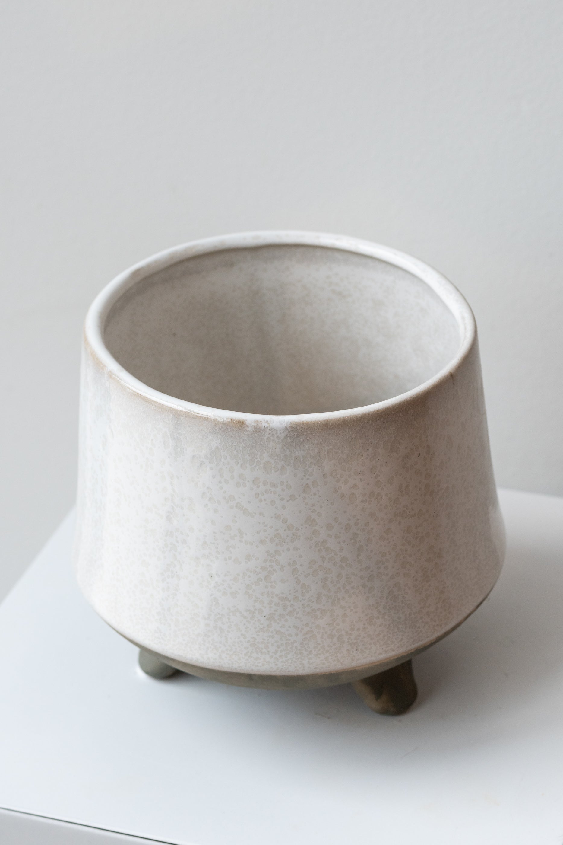 Glazed white stoneware planter with unglazed grey feet and base sits on a white surface in front of a white background