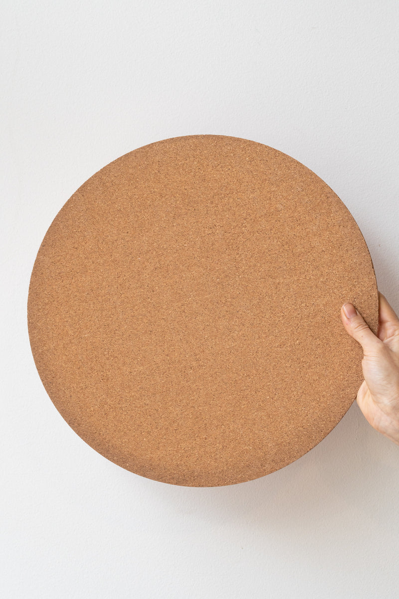 Hand holding 14-inch round cork mat in front of white background