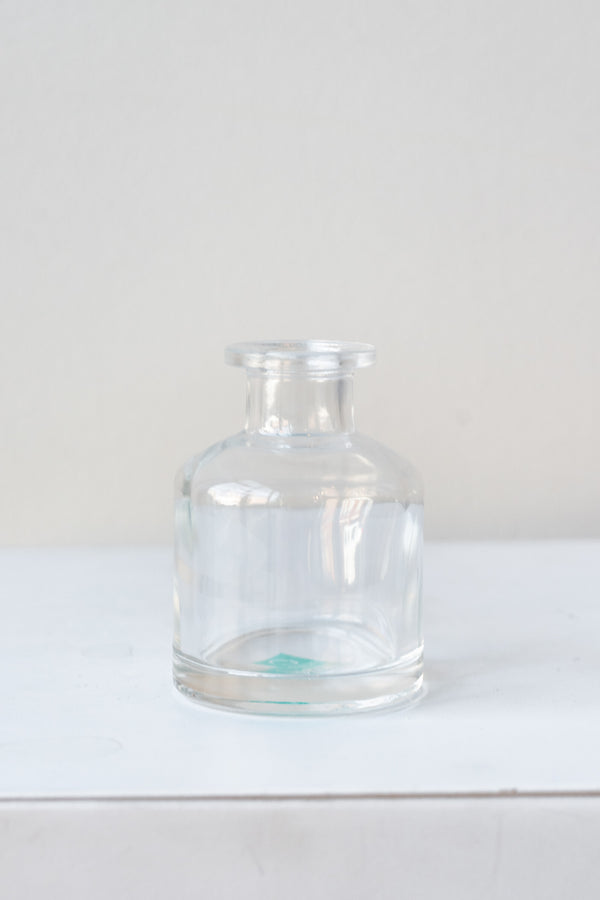 Small clear bottle vase sits on a white surface in a white room