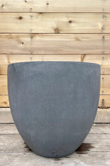 Jesslyn Pot Fiberstone grey medium against a wooden fence