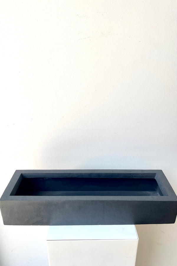 A slight overhead view of the slim, low, black balcony planter in small against a white backdrop