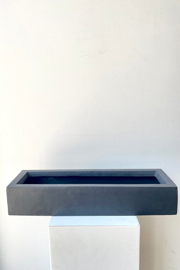 A frontal view of the slim, low, black balcony planter in small against a white backdrop
