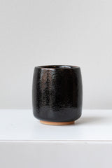 Black Tenmoku Cup by Miya Company Inc sits on a white surface in a white room