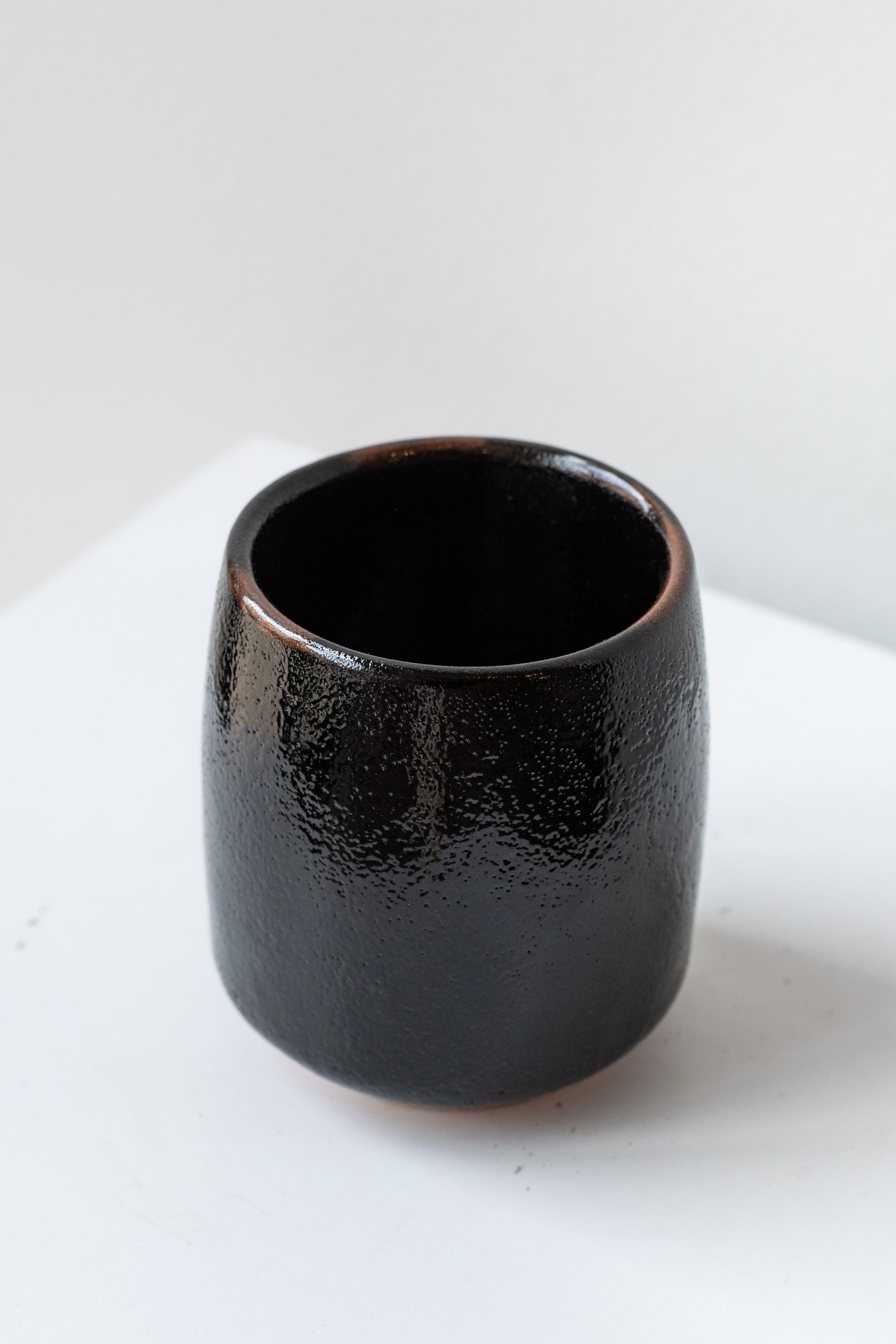 Black Tenmoku Cup by Miya Company Inc sits on a white surface in a white room