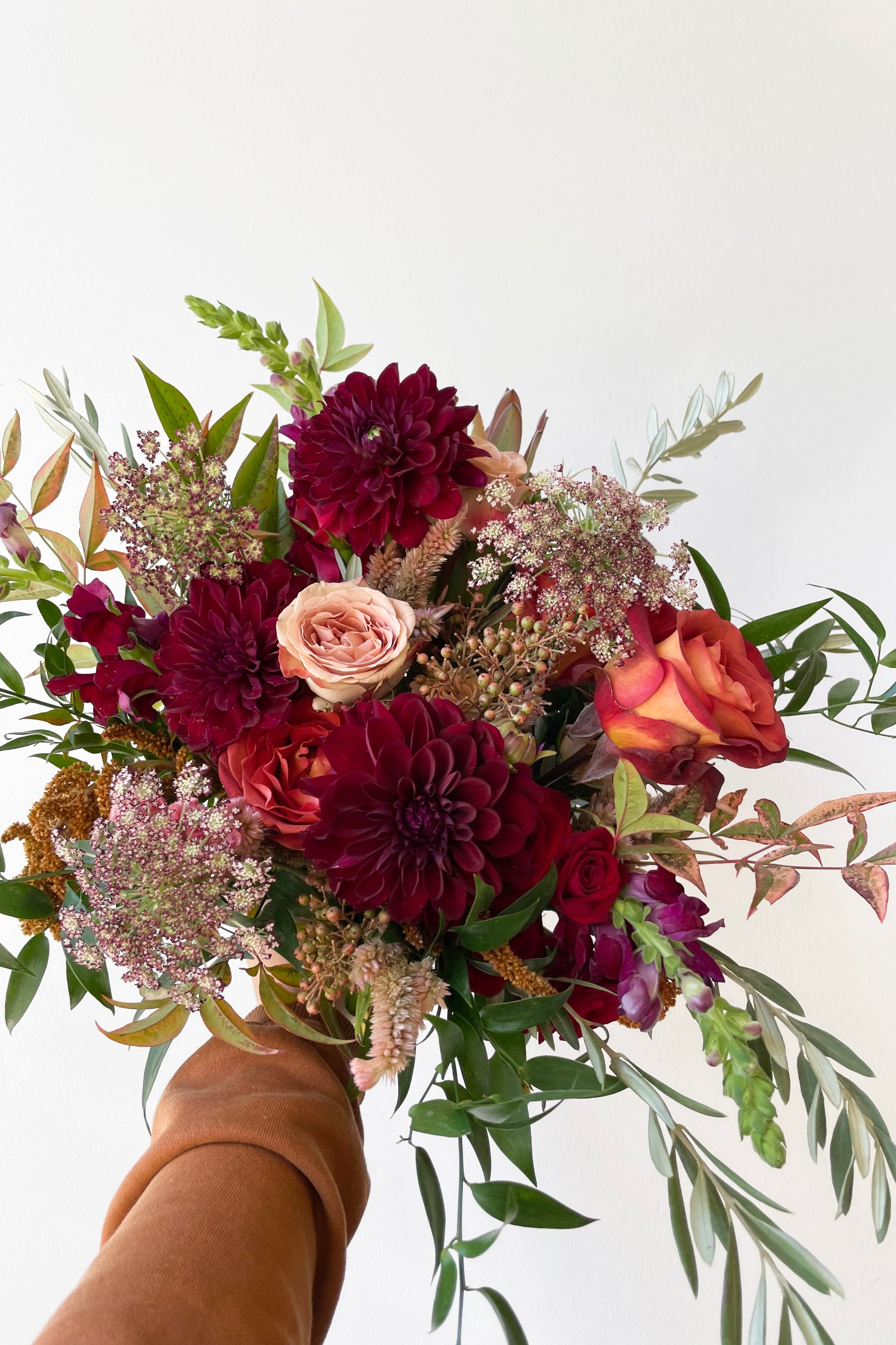 A hand holds an example of fresh Floral Arrangement Earth with burgundy Dahlia from Sprout Home Floral ©Sprout Home #size_$130
