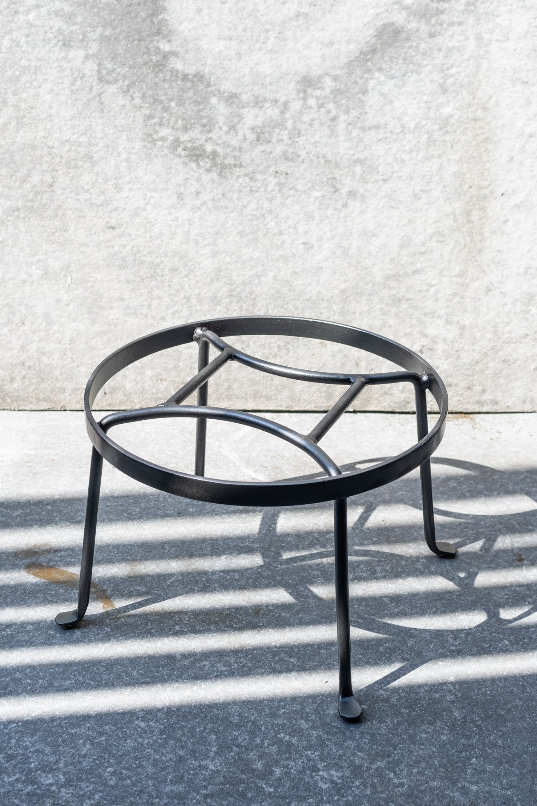 The small Argyle plant stand shown against a grey wall with the sunlight hitting it,. 